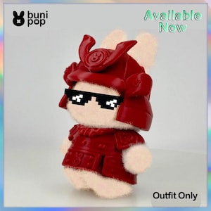 May include: A plush toy bunny wearing a red samurai helmet and armor, with pixelated sunglasses. The image includes the text "Available Now" and "Outfit Only". The bunny has a white body and ears, and the outfit is a deep red.