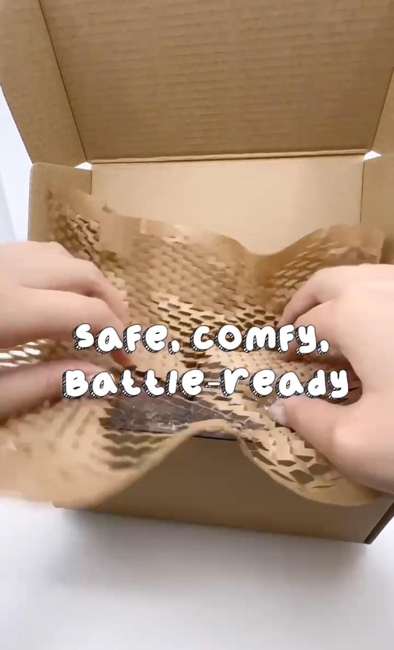 May include: A cardboard box with brown packing material and the text "safe, comfy, battle-ready". The box is open, and hands are shown arranging the packing material.