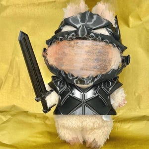 Könnte beinhalten: Ein Stofftier-Hamster in schwarzer Rüstung und Helm, der ein schwarzes Schwert hält. Der Hamster hat helles Fell und befindet sich vor einem gelben Hintergrund.