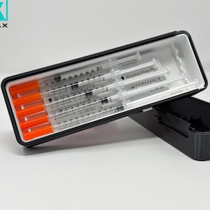May include: A black rectangular case with a white interior, holding several syringes with orange caps. The case is open, revealing the contents, and the brand name "CALVORAX" is visible in the upper left corner.
