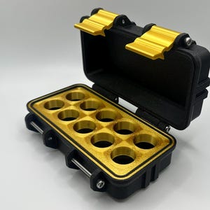 May include: Black and gold storage case with a hinged lid. The interior features a gold-colored tray with nine circular compartments. The case has gold-colored latches and hinges, and is open to display the contents.