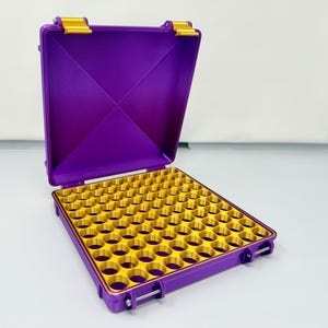 May include: Open purple case with gold-colored interior and hinges. The case is rectangular with a grid of circular holes inside. The case is open, revealing the interior. The hinges and clasps are gold.