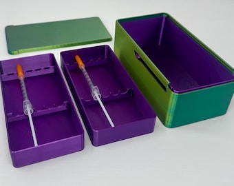 May include: A set of purple and green storage containers with a lid. The containers have a rectangular shape and are designed to hold medical syringes. The syringes have orange caps.