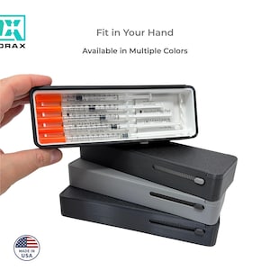 May include: A black case with a sliding mechanism, stacked on top of two other cases in gray and black. The top case is open, revealing syringes with orange caps. Text reads "Fit in Your Hand" and "Available in Multiple Colors."