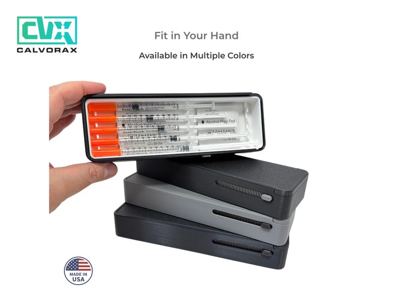 May include: A black case with a sliding mechanism, stacked on top of two other cases in gray and black. The top case is open, revealing syringes with orange caps. Text reads "Fit in Your Hand" and "Available in Multiple Colors."