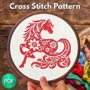 May include: A cross stitch pattern featuring a red horse silhouette filled with white floral motifs on white fabric, held in a circular wooden embroidery hoop. The text Cross Stitch Pattern is at the top and a green PDF badge is at the bottom left.