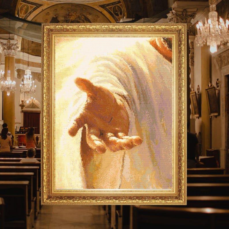 May include: A framed cross-stitch artwork depicting a close-up of an outstretched hand reaching forward, rendered in soft shades of white, cream, and tan. The image is encased in an ornate, metallic gold rectangular frame with intricate carvings.