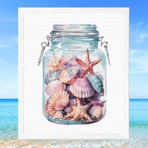 May include: A framed cross-stitch design shows a glass jar filled with seashells and starfish. The shells are in shades of pink, peach, and blue, with several orange starfish. The jar has a metal clasp and lid, set against a backdrop of a blue sky and ocean.
