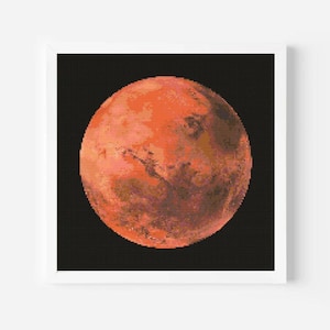 May include: A framed cross-stitch of the planet Mars, rendered in shades of orange, red, and brown. The detailed stitching depicts the planet's surface against a black background, framed in a white square.