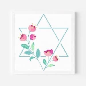 May include: A framed cross-stitch design featuring a light blue Star of David with a floral arrangement. The flowers are pink with yellow centers, and the leaves are green. The frame is white.