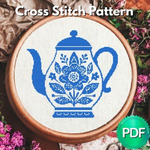 以下が含まれることがあります： 白い布に青いティーポットと花柄が刺繍されたクロスステッチパターンで、丸い木製の刺繍枠に収められています。上部にはCross Stitch Patternの文字があり、隅には緑色の円形のPDFバッジが表示されています。