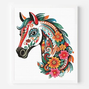 May include: A framed cross-stitch depicting a horse's head, adorned with vibrant floral and paisley designs. The colour palette includes red, orange, blue, and green. The mane and neck are embellished with flowers. The background is white.