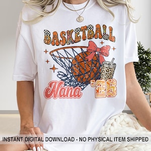 Può includere: T-shirt bianca con grafica a tema basket. Il design include la scritta "Basketball" in arancione e nero a scacchi, un pallone da basket, una rete e la scritta "Nana" in rosso. Sono presenti anche una tazza con stampa leopardata e il numero "73".
