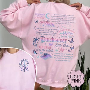 May include: Pale pink sweatshirt with the word "Quicksilver" and other graphics. The back of the sweatshirt features text and illustrations of butterflies, mountains, and other designs. The front of the sweatshirt has a smaller version of the "Quicksilver" design.