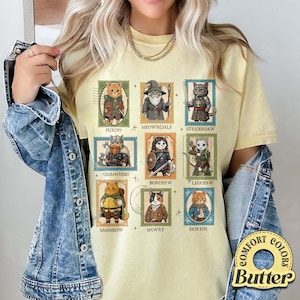 K&ouml;nnte beinhalten: Hellgelbes T-Shirt mit neun Katzenillustrationen in Briefmarkendesigns. Jede Katze ist als Figur mit Namen wie Furdo, Meowndalf und Striderpaw gekleidet. Das Shirt hat ein Comfort Colors Butter-Label.