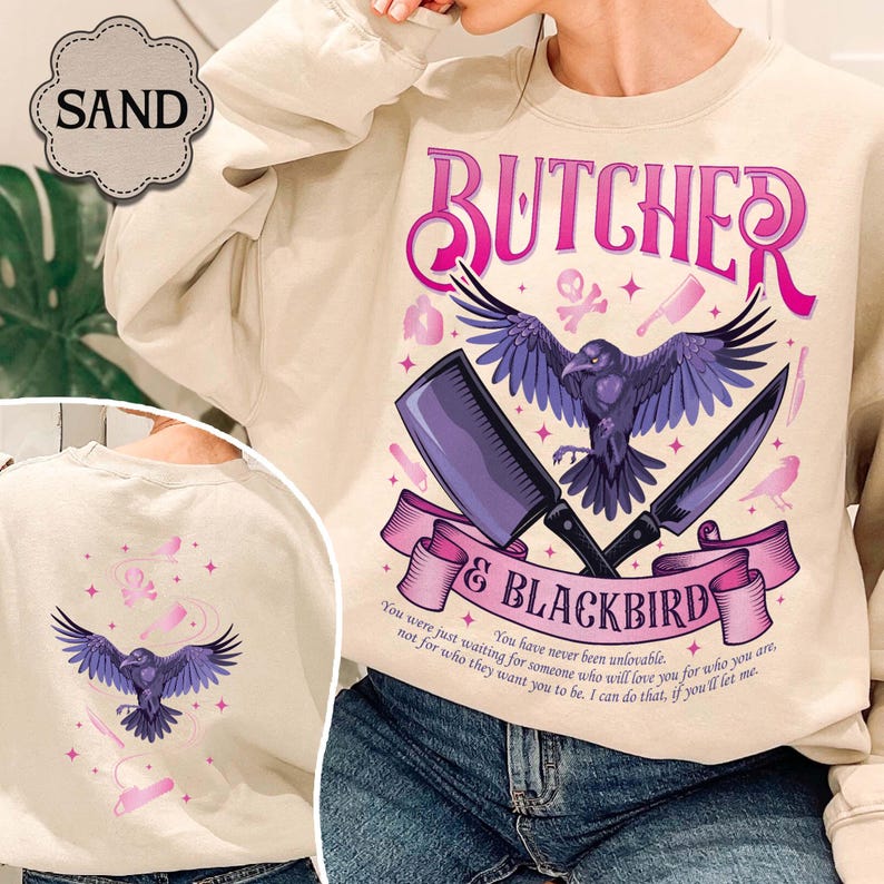 May include: Sand-colored sweatshirt with a graphic design featuring a raven, cleaver, and knife. The text reads "BUTCHER & BLACKBIRD" with additional text below. The back of the sweatshirt also features a raven design.