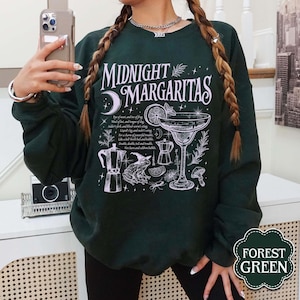 May include: Forest green sweatshirt with the text "MIDNIGHT MARGARITAS" in white. The design includes a margarita glass, a moon, and other illustrations. The sweatshirt is a solid color and has a crew neck.