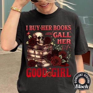 May include: Black t-shirt with a graphic design featuring a skull atop a stack of books, surrounded by red roses. The text reads "I BUY HER BOOKS and GALL HER A GOOD GIRL."