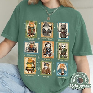K&ouml;nnte beinhalten: Hellgr&uuml;nes T-Shirt mit Illustrationen von Katzen in Fantasy-Kost&uuml;men, jeweils in einem Poststempel-&auml;hnlichen Rahmen. Das Shirt zeigt die Namen "FURDO", "MEOWNDALF", "STRIDERPAW", "GRIMWHISH", "BOROPAW", "LEGOPAW", "SAMMEOW", "MEWRY" und "PAWPIN".