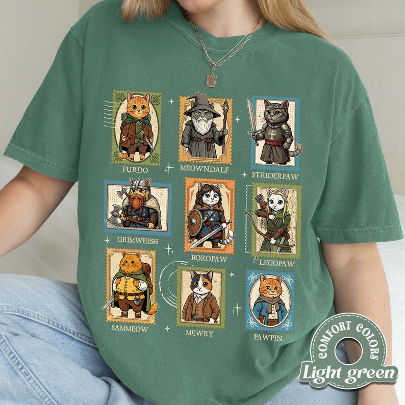 K&ouml;nnte beinhalten: Hellgr&uuml;nes T-Shirt mit Illustrationen von Katzen in Fantasy-Kost&uuml;men, jeweils in einem Poststempel-&auml;hnlichen Rahmen. Das Shirt zeigt die Namen "FURDO", "MEOWNDALF", "STRIDERPAW", "GRIMWHISH", "BOROPAW", "LEGOPAW", "SAMMEOW", "MEWRY" und "PAWPIN".