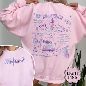 May include: Light pink sweatshirt with a graphic design featuring the word "Kingfisher", a sword, mountains, butterflies, and the text "Quicksilver". The back of the sweatshirt has additional text and illustrations.