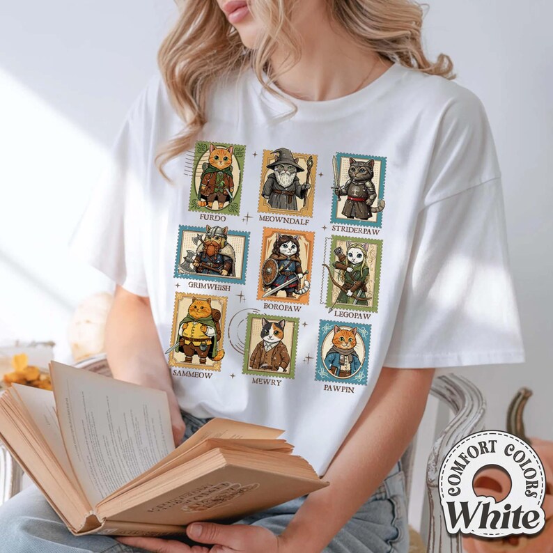 K&ouml;nnte beinhalten: Wei&szlig;es T-Shirt mit einer Reihe von Katzenillustrationen, die als Briefmarken gestaltet sind. Jede Briefmarke zeigt eine Katze in einem Kost&uuml;m mit einem Namen. Das T-Shirt tr&auml;gt auch den Text "COMFORT COLORS White".