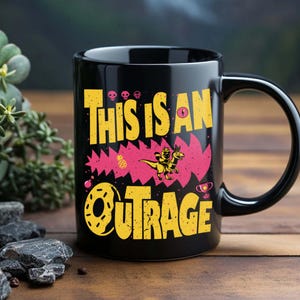 May include: Black ceramic mug with a yellow and pink graphic. The mug features the text "THIS IS AN OUTRAGE" in yellow, along with a cartoon dinosaur riding a dinosaur. A pineapple, skulls, and a trophy are also included in the design.