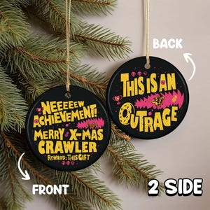 May include: Two-sided black Christmas ornament with gold string. The front reads "NEEEEEW ACHIEVEMENT! MERRY X-MAS CRAWLER REWARD: THIS GIFT" in yellow and pink. The back says "THIS IS AN OUTRAGE" in yellow and pink. The ornament is hanging on a green Christmas tree.