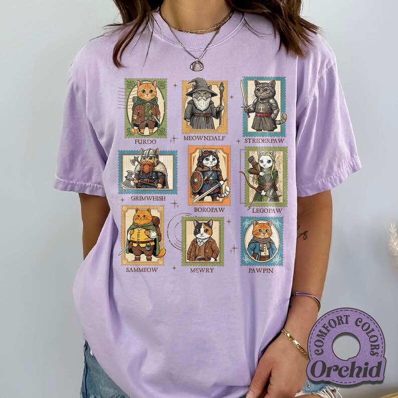 K&ouml;nnte beinhalten: Ein helllila T-Shirt mit neun Katzenillustrationen, die als Briefmarken gestaltet sind. Jede Katze ist in Fantasy-Kleidung gekleidet, mit Namen wie "Sammeow" und "Mewry". Das Shirt hat ein Comfort Colors Orchid-Label.