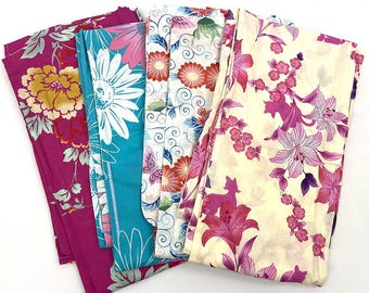May include: A collection of folded floral fabric pieces in various colors. The fabrics feature large flower patterns in shades of pink, yellow, blue, and white. The fabrics are likely for sewing or crafting.