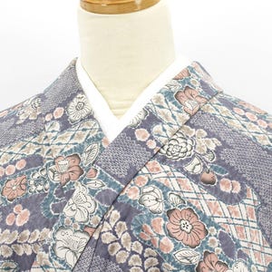 Puede incluir: Primer plano de un kimono con un estampado floral en tonos morado, rosa y blanco. El kimono presenta un diseño geométrico y un cuello blanco. La tela parece suave y fluida.
