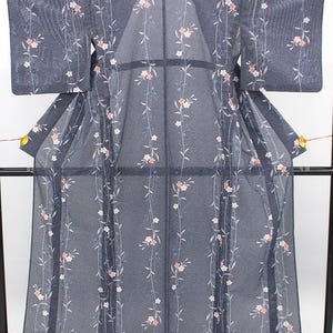 May include: A dark blue kimono featuring a fine white dotted pattern and vertical trailing vines with small light pink and white flowers. The garment has wide sleeves and a sheer, lightweight texture, displayed on a black frame.