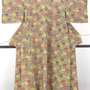 May include: A kimono featuring a vibrant, all-over pattern of interlocking hexagonal shapes in shades of lime green, red, navy blue, and white. The fabric displays a dense, repeating geometric design with small circular motifs scattered throughout the garment.