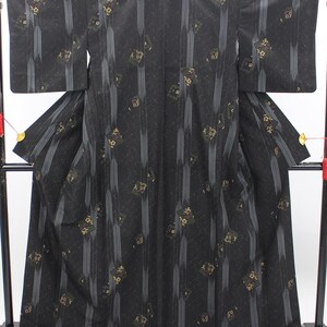 May include: A black kimono featuring vertical grey pinstripes and scattered square-shaped patterns containing gold and white floral motifs. The garment has wide sleeves and a structured silhouette, displayed flat against a dark frame.