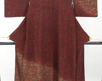 May include: A deep red kimono featuring an intricate, repeating geometric and floral pattern throughout the fabric. The garment displays a darker, shaded gradient effect along the lower hem and sleeve edges, with wide sleeves and a structured silhouette.