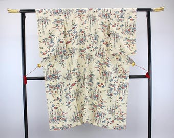 May include: A cream-colored kimono with a floral pattern in red, blue, and green. The garment is displayed on a black metal rack with gold accents. The kimono's design features stylized birds and botanical elements.