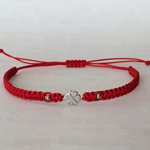 May include: Red braided bracelet with a silver four-leaf clover charm and two silver beads. The bracelet is adjustable with a sliding knot closure. A simple and elegant piece of jewellery.