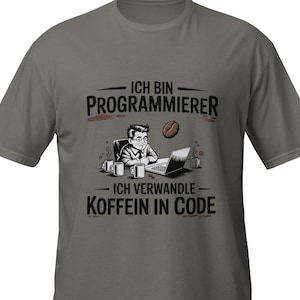 Könnte beinhalten: Graues T-Shirt mit einer Grafik, die einen Programmierer an einem Laptop, Kaffeetassen und eine Kaffeebohne zeigt. Der Text lautet "ICH BIN PROGRAMMIERER" und "ICH VERWANDLE KOFFEIN IN CODE."