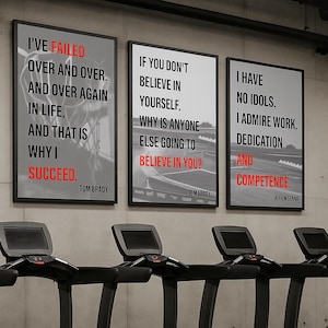 Op de afbeelding: Drie ingelijste motiverende posters met zwarte frames en witte achtergronden. De posters bevatten citaten van Tom Brady en Ayrton Senna in zwarte en rode tekst. Loopbanden zijn zichtbaar op de voorgrond.