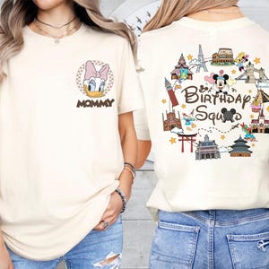 May include: Cream-colored t-shirt featuring a Daisy Duck graphic with a pink bow and the word "MOMMY" on the front. The back of the shirt displays a colorful "Birthday Squad" design with iconic landmarks and Disney characters.
