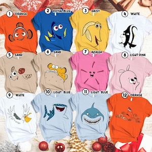 May include: A collection of twelve short-sleeved t-shirts in various colors, each featuring a cartoon character design. Colors include orange, royal blue, yellow, white, sand, light pink, and light blue. The shirts are arranged in a grid.