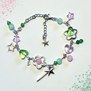 May include: A silver-toned bracelet featuring a whimsical design with various charms. The bracelet includes star, heart, and flower-shaped charms, along with green, pink, and clear beads. A silver wand charm hangs from the bracelet.