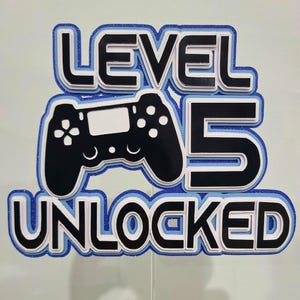 May include: A white ceramic mug with a black handle and the text "But First, Coffee" in a bold, black font. The mug is set against a blurred background. The mug appears to be approximately 10 cm tall.