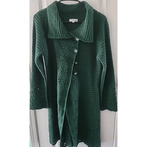 Può includere: Un cappotto all'uncinetto verde scuro a maniche lunghe, con ampio colletto e chiusura con bottoni. Il cappotto presenta un motivo strutturato e dettagli traforati sulle maniche e sul davanti. Il cappotto è lungo circa 102 cm.