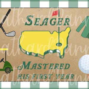 Puede incluir: Un diseño con temática de golf con palos de golf cruzados, un carrito de golf, una pelota de golf y una chaqueta verde. El diseño incluye un contorno amarillo de los Estados Unidos con una bandera de golf y el texto "Seager Mastered His First Year."