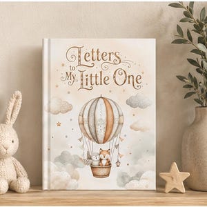 Può includere: Un libro per bambini intitolato "Letters to My Little One" con un'illustrazione di mongolfiera, nuvole e animali del bosco. Un coniglietto di maglia, una stella di legno e un vaso con piante sono anch'essi presenti.