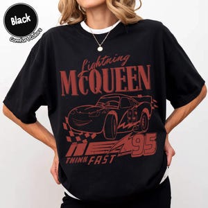 K&ouml;nnte beinhalten: Schwarzes T-Shirt mit roter Grafik von Lightning McQueen aus dem Film Cars. Das Design enth&auml;lt den Text "Lightning McQueen", die Nummer "95" und den Satz "Think Fast". Das Shirt ist im Comfort-Colors-Stil.