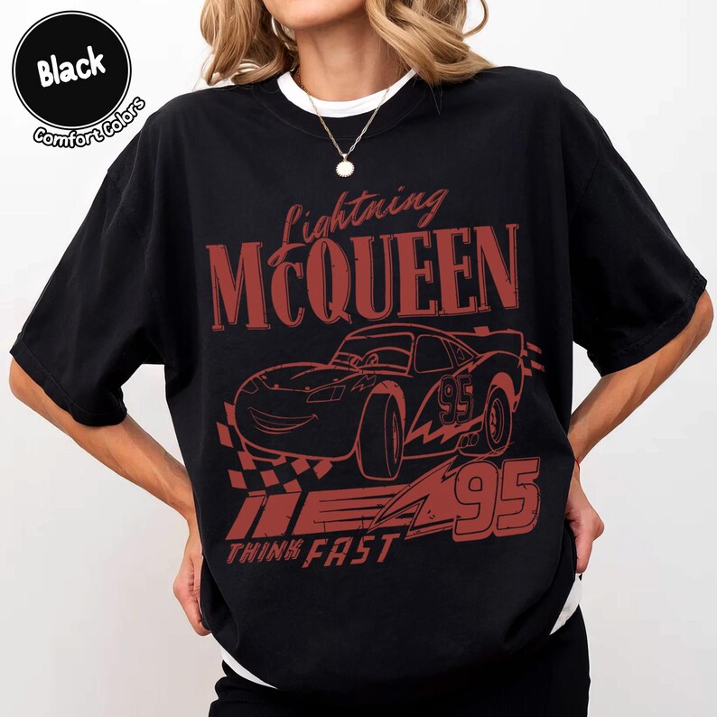 K&ouml;nnte beinhalten: Schwarzes T-Shirt mit roter Grafik von Lightning McQueen aus dem Film Cars. Das Design enth&auml;lt den Text "Lightning McQueen", die Nummer "95" und den Satz "Think Fast". Das Shirt ist im Comfort-Colors-Stil.