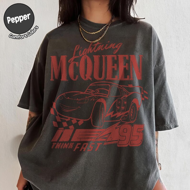 K&ouml;nnte beinhalten: Dunkelgraues T-Shirt mit roter Grafik von Lightning McQueen aus dem Film Cars. Das Design enth&auml;lt den Text "Lightning McQueen", "95" und "Think Fast". Das Shirt hat eine lockere Passform und kurze &Auml;rmel.