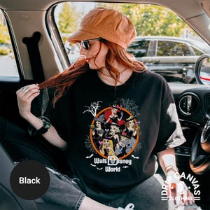Puede incluir: Camiseta negra con un dise&ntilde;o de Halloween con personajes de Disney con sombreros de bruja. El dise&ntilde;o est&aacute; dentro de un c&iacute;rculo naranja con telara&ntilde;as y el texto "Walt Disney World".